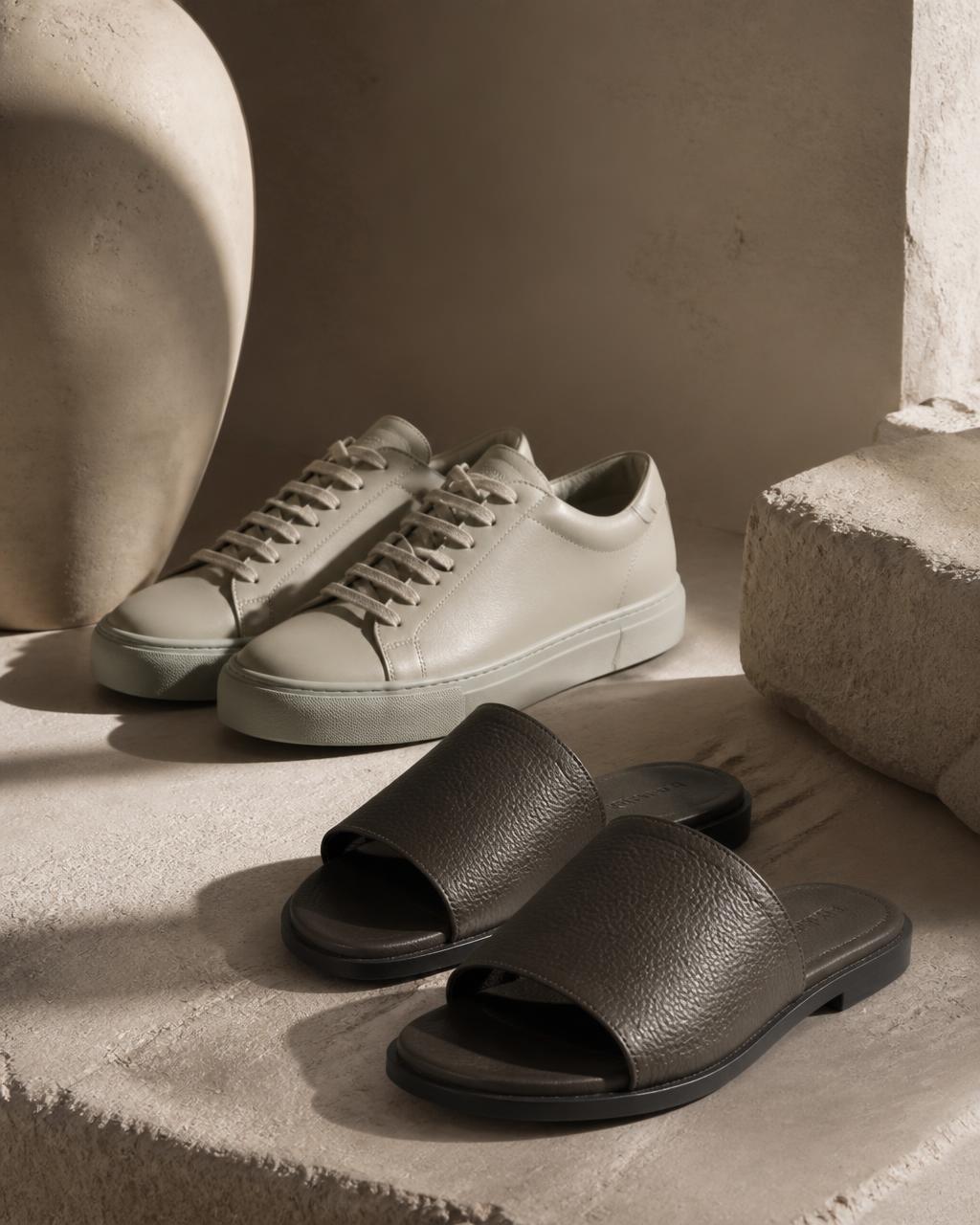 Minimal leather sneakers and slides on a soft stone surface